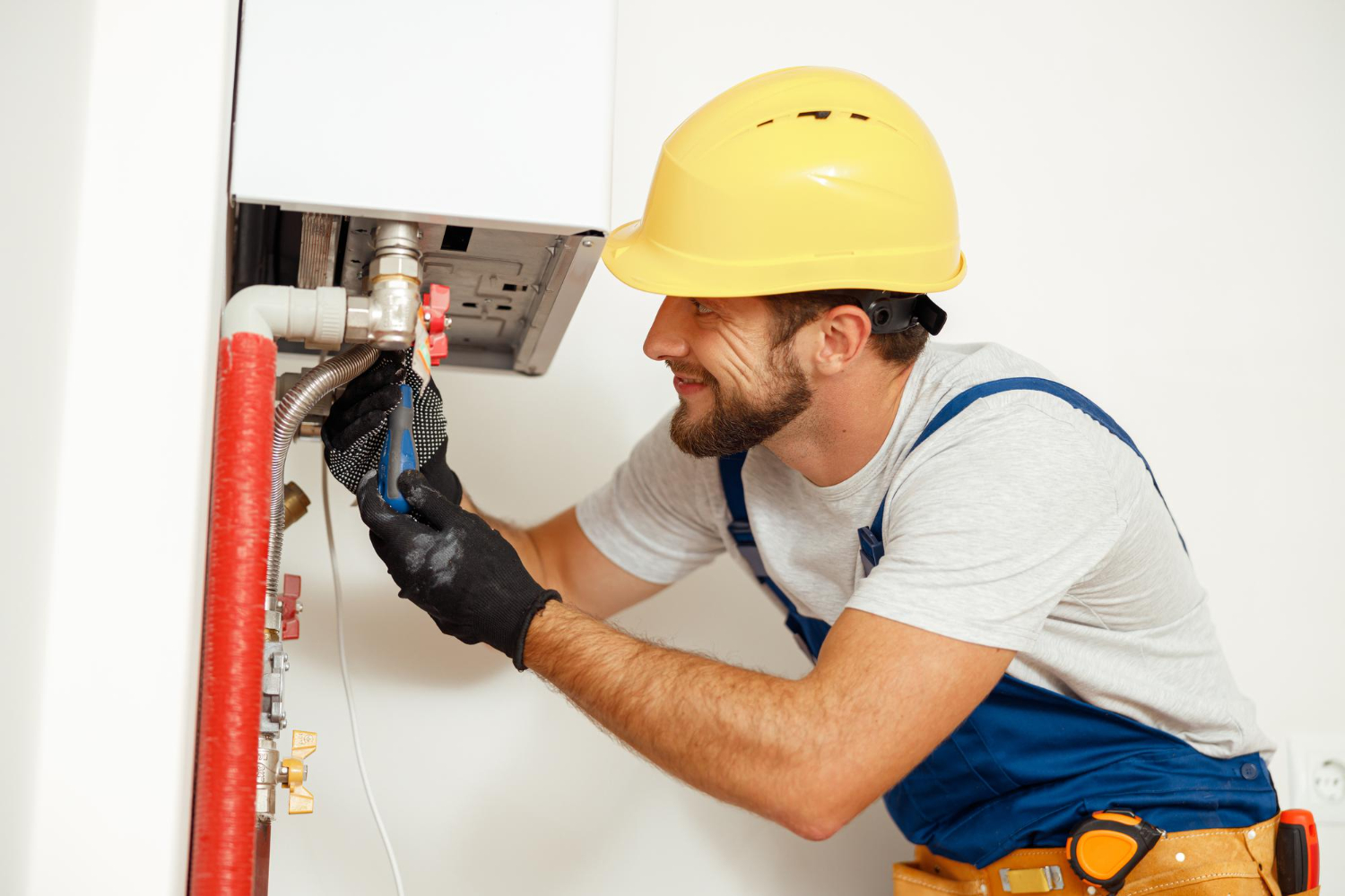HVAC technician repairing a gas water heater, wearing a yellow hard hat and gloves, with tools in hand, illustrating maintenance services relevant to Easton homeowners.
